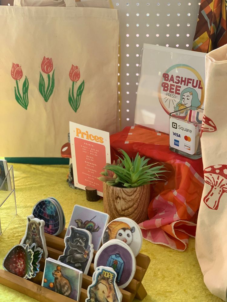 Tulip and mushroom tote bags and stickers in foreground 