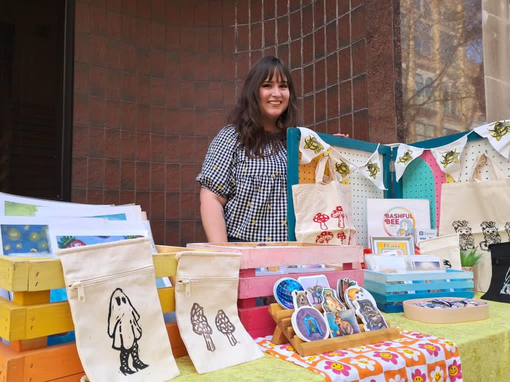 Picture of woman with brown hair at a table of merchandise. 