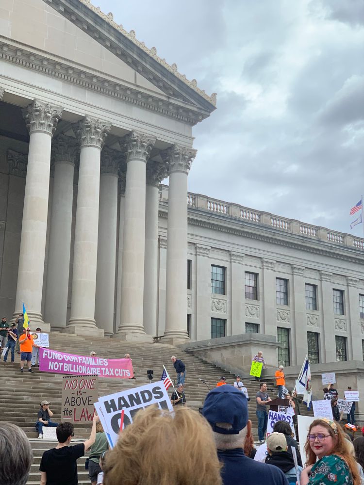 WV State Capitol building exterior with protestors holding signs 