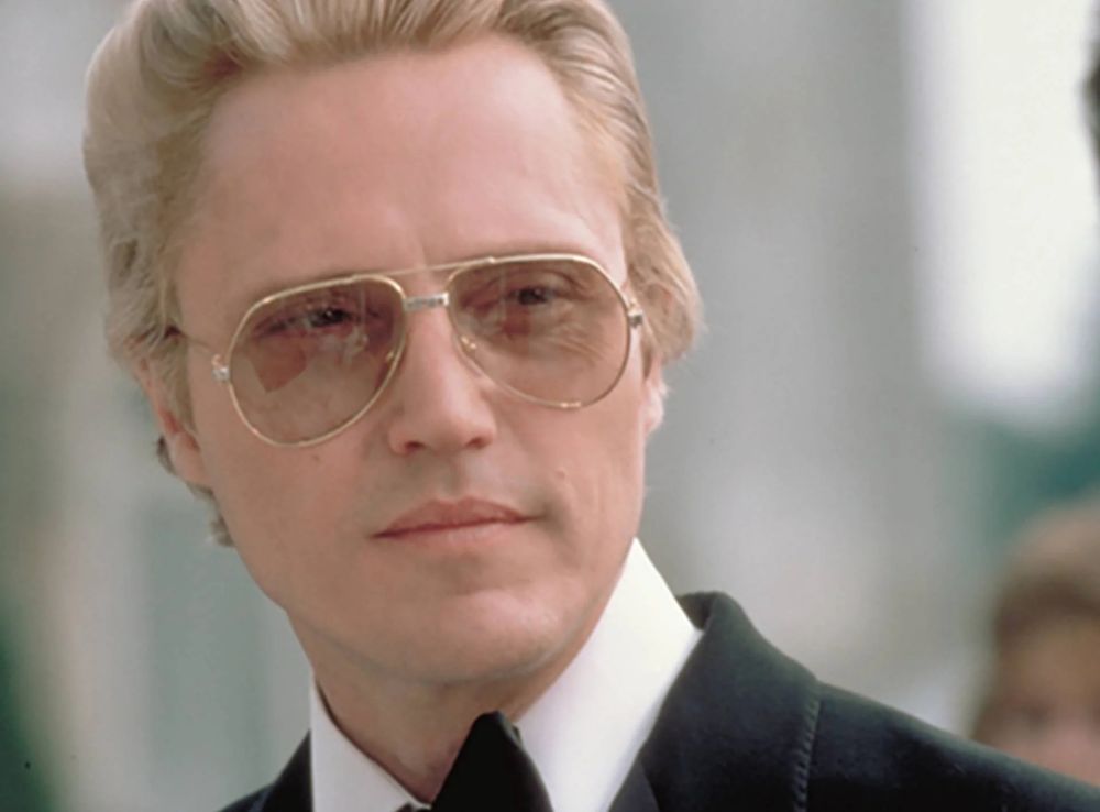 The face of James Bond villain Max Zorin from "A View to a Kill", as played by Chrisopher Walken wearing 80s sunglasses, a black suit and tie, and with dyed blonde hair