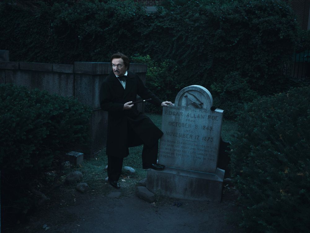 Man dressed as Edgar Allan Poe standing at Poe’s grave in Baltimore in the night