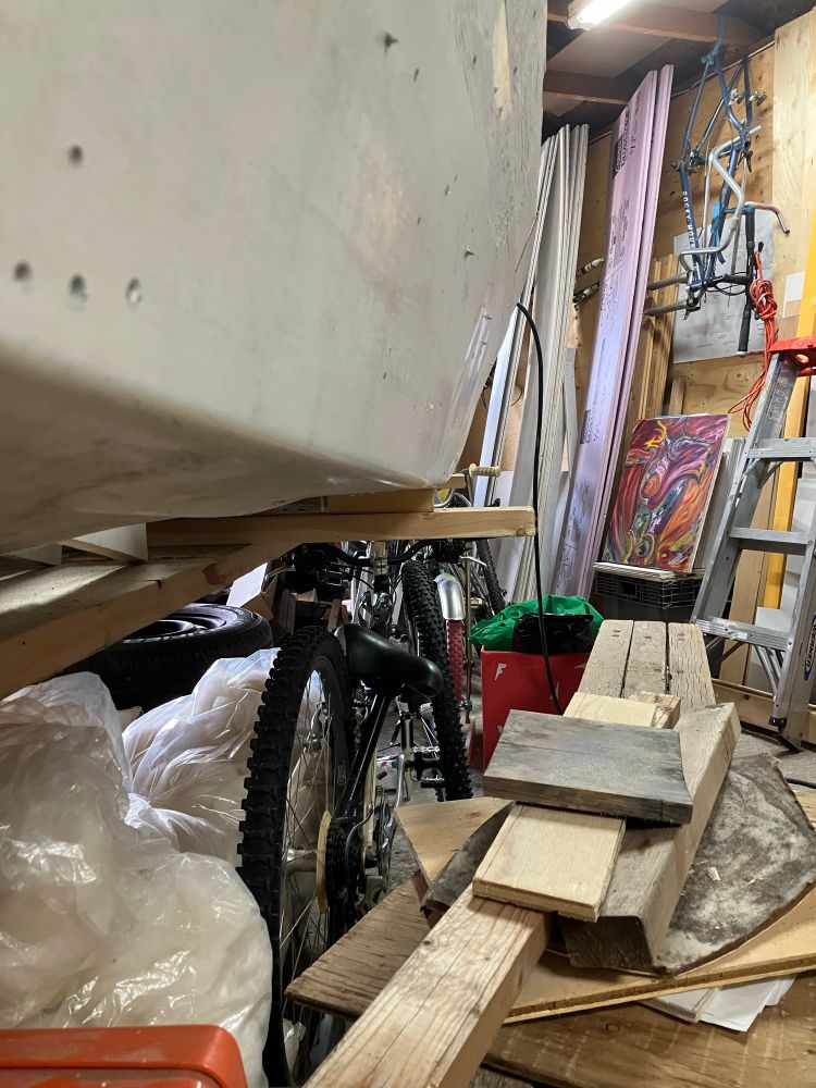 a close up photograph showing the lower and underside of a fiberglass kayak on a support with multiple bicycles in view as well as wood debris, wool, a painting, and work materials. I am coming to the realization that This Project is affirmation of possibilities.. the possibilities of life that were stolen from me due to multifarious firms of abuse causing *sometimes* crushing disbelief in My Self.. so, while TheBoat (nicknamed Tooker) probably could have been pulled off her cradle awhile ago.. my fear was that my build wouldnt be *good enough* and, when removed from the sort-of supportive cradle, she'd collapse. That was also partly why, when i discovered the boat named 'Atlantelia' as a finished ocean row boat for sale.. i figured i could skip a bunch of steps and be on my way in her, safe and sound. Not so.. the design of Atlantelia is highly questionable.. so, make progress on 'Tooker' .. keep on, jeeping on.

long story short.. pulling off the cradle was uplifting. To see my work at a new level, to see her without splints and supports.. and to see her ready for the next phase is absolutely and incredibly exciting. 

to make a long story, longer.. the cradle was a two- by- four superstructure that was built in two halves.. or, built around TheBoat being halved up.. so, there was the Bow section and Stern section.. these sat on two by four 'rails' that had wooden channels set up so it could only move in one direction.. longer. Once TheBoat was cut in half, i pulled her to 22' in length and added plywood to keep her rigid.

Now, the rails and cradle are completely gone.. and their wood (two by fours, too big for my uses) will go to my current #yyc host and old friend and visionary confidant.