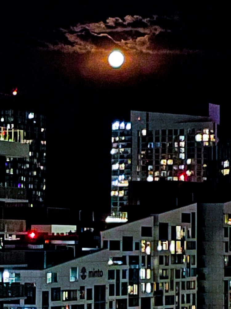 Hazy photo of full moon over city buildings. 