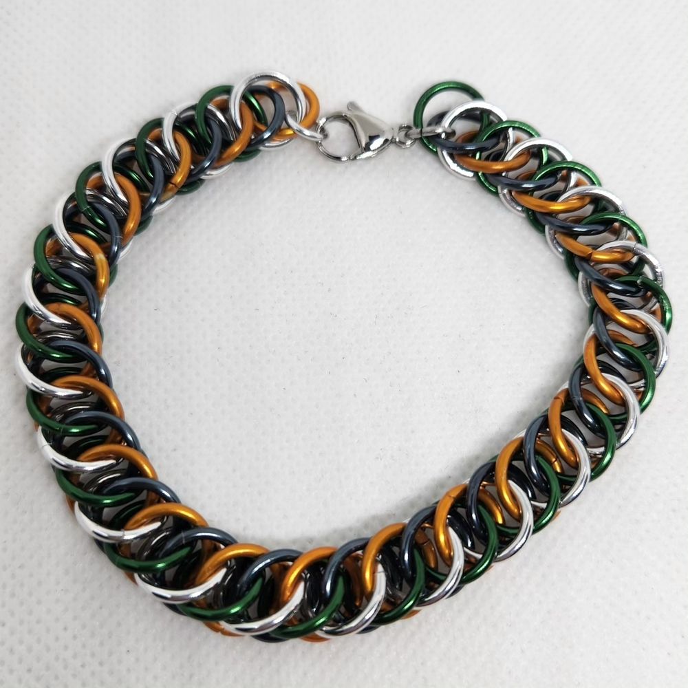 Chainmail bracelet in half Persian 4 in 1 weave, alternating green and silver on one side, orange and black on the other