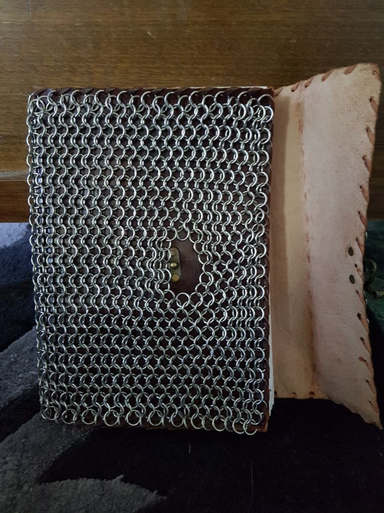 A leather book covered in stainless steel chainmail, the right cover flap open to reveal the underside of the leather.