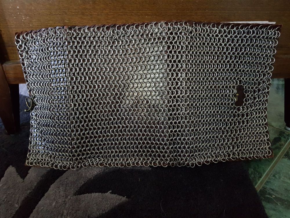 The back side of a fully open leatherbound book covered in stainless steel chainmail