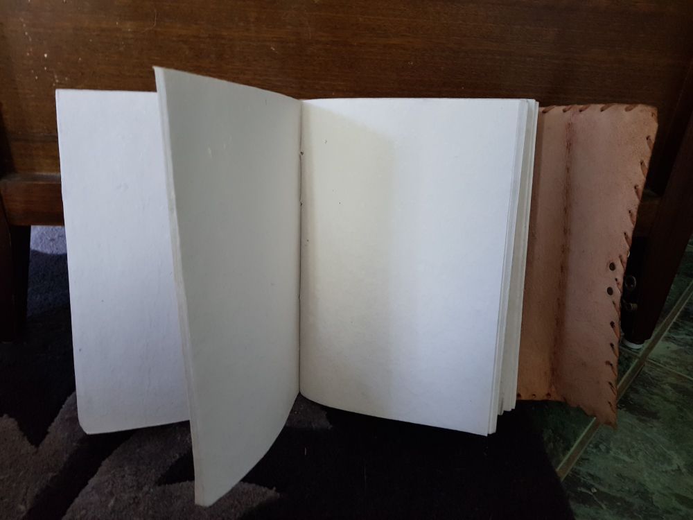 An open leatherbound book showing blank pages and the leather side flap