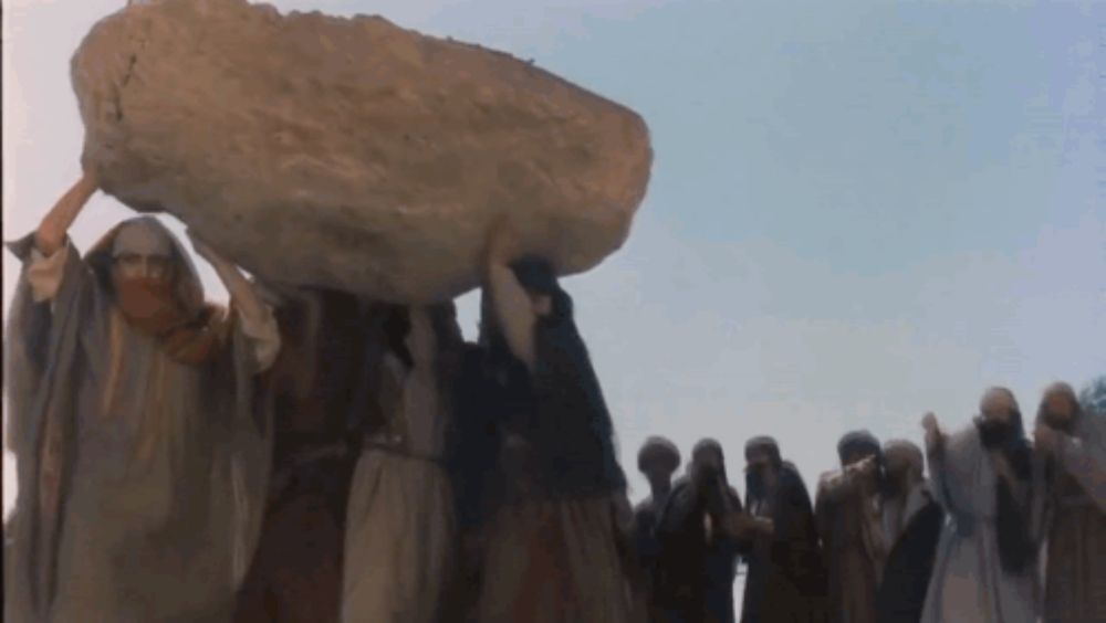 a group of people are carrying a large rock on their heads