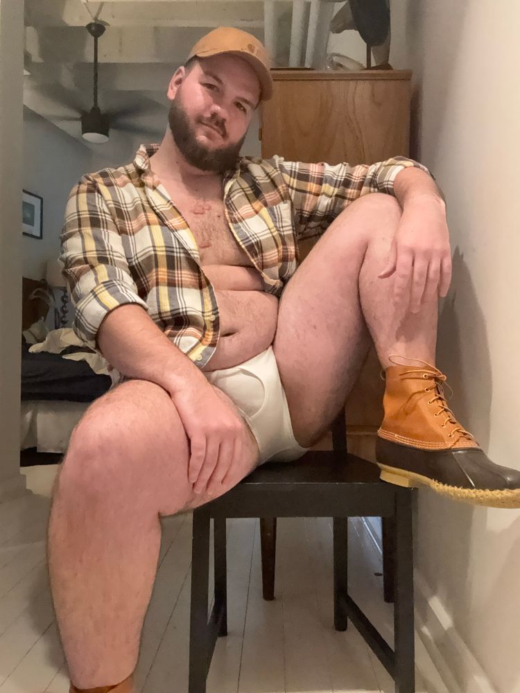 Photo of me sitting on a chair in a flannel and white briefs wearing brown duck boots 