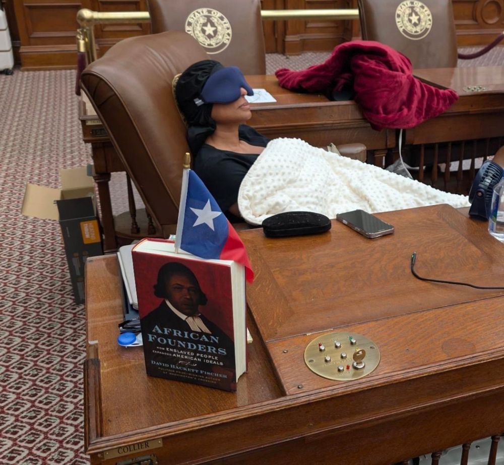 Rep. Nicole Collier in the Texas House chamber asleep in a chair at her desk wearing an eye mask and with a blanket pulled over herself.

Prominently placed, a hardcover book with the flag of Texas jammed in between its pages stands upright.

The book is historian David Hackett Fischer's American Founders: How Enslaved People Expanded American Ideals.