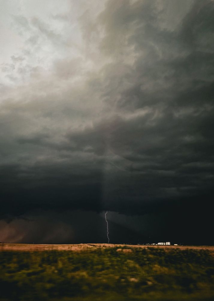 Dark stormy skies from a distance over a farm in a field, with a lightning strike hitting the ground