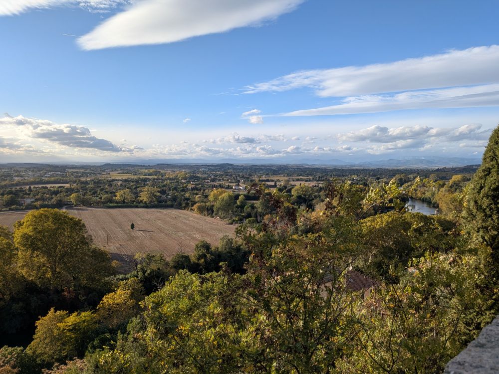 Vue sur l'Orb et sa plaine cultivée et arborée, avec les monts du Caroux et de l'Escandorgue dans l'arrière pays héraultais, sous un ciel majoritairement bleu avec des nuages lenticulaires traduisant une "légère" tramontane.