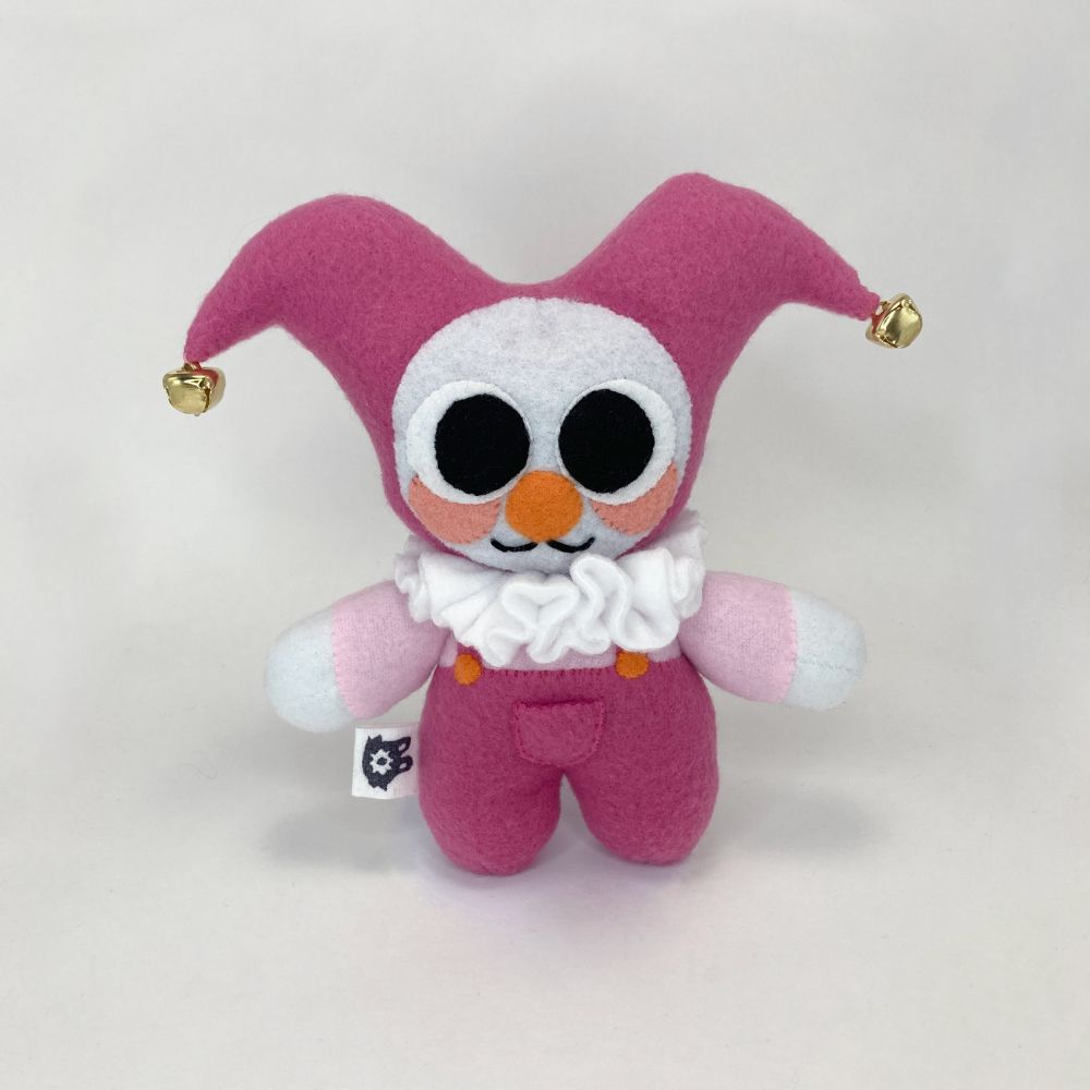 photo of a clown plushie with a pink color palette with huge eyes and bells on the end of their jester hood.