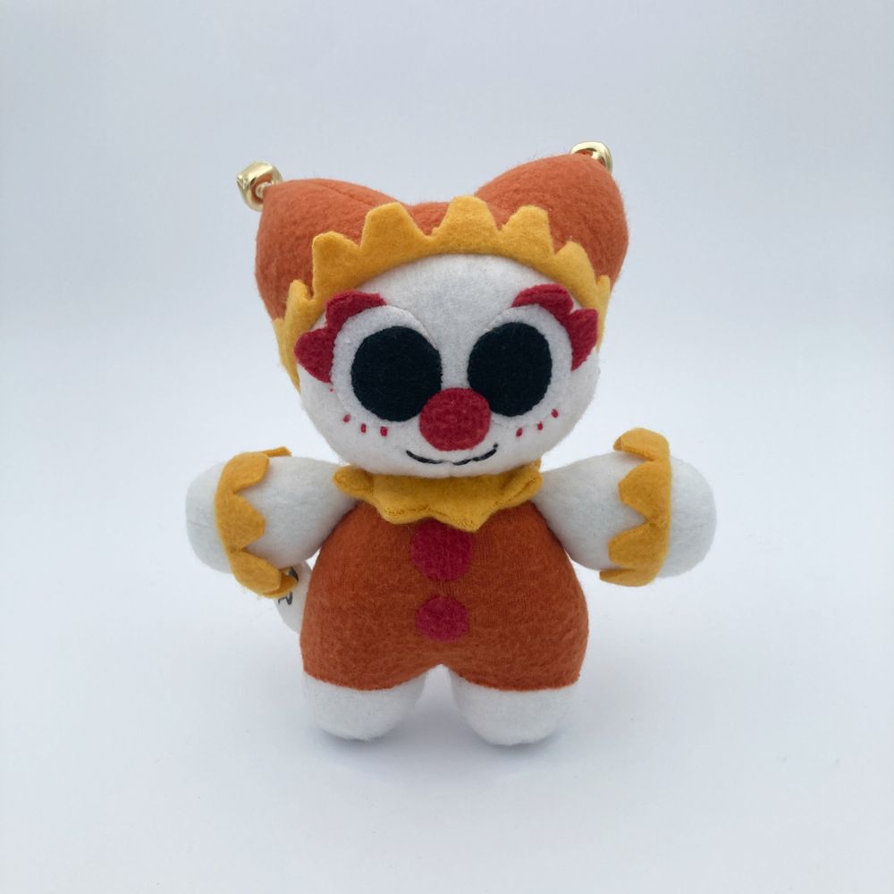 photo of a clown plushie with a red, orange, and yellow color palette. the clown is wearing a jester hat with bells on the end.