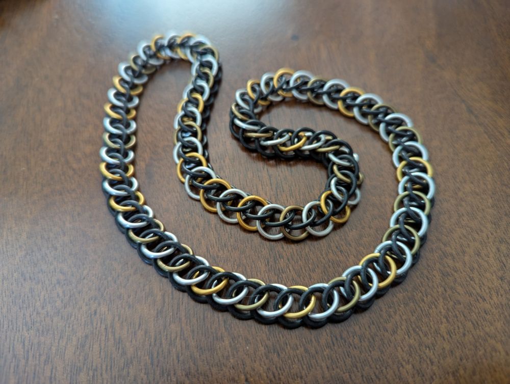 Photo of a chainmail necklace in black, silver, gold, and olive