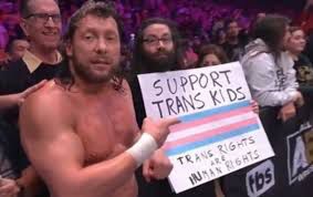 Kenny Omega from AEW stands next to a "Support Trans Kids, Trans Rights Are Human Rights" sign and says "You know it, I know it, everybody should know it"