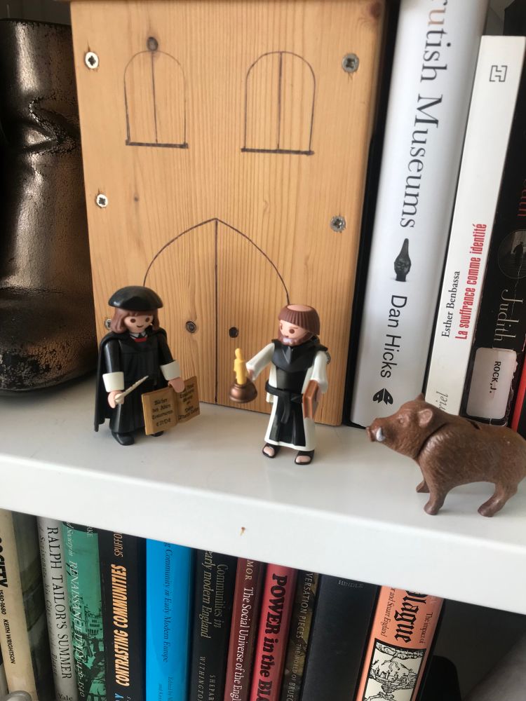 Picture of a book shelve with two playmobil figurines. One is Luther, the other a tonsured (really) monk.  