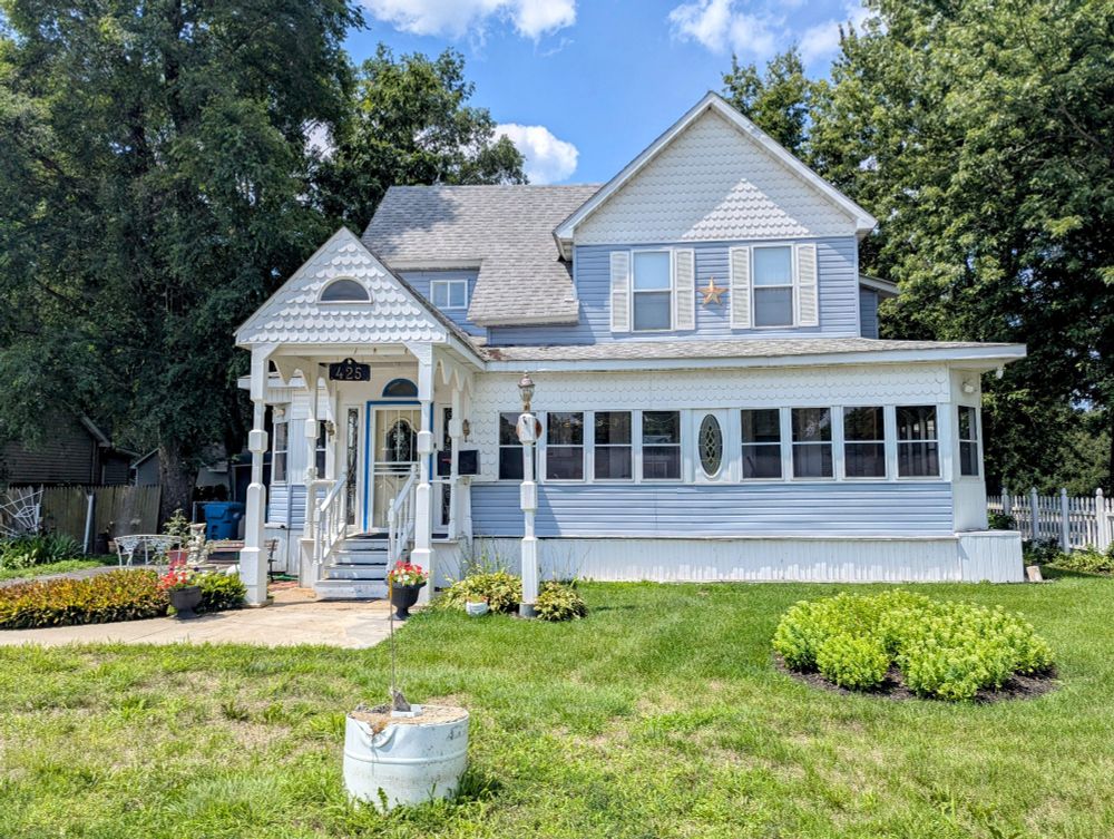 Photo of a two-story house with wood and some vinyl siding in white and I think a pale purple.