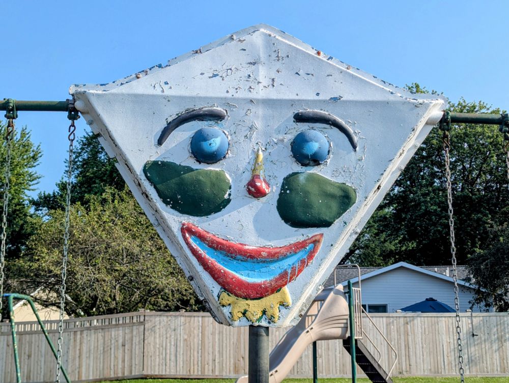 Close up photo of a white painted diamond with peeling paint and a brightly colored clown face on it.