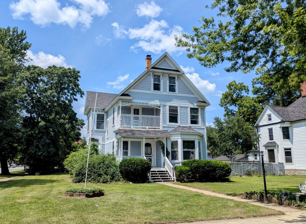 Photo of a three-story house with Victorian characteristics and white trim and light blue wooden siding.