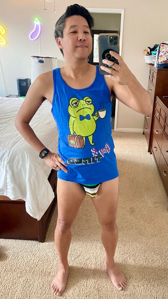 Me in a blue tank top with a tired frog holding a cup of coffee with text Gay &Tired. Also wearing a pair of briefs with stripes