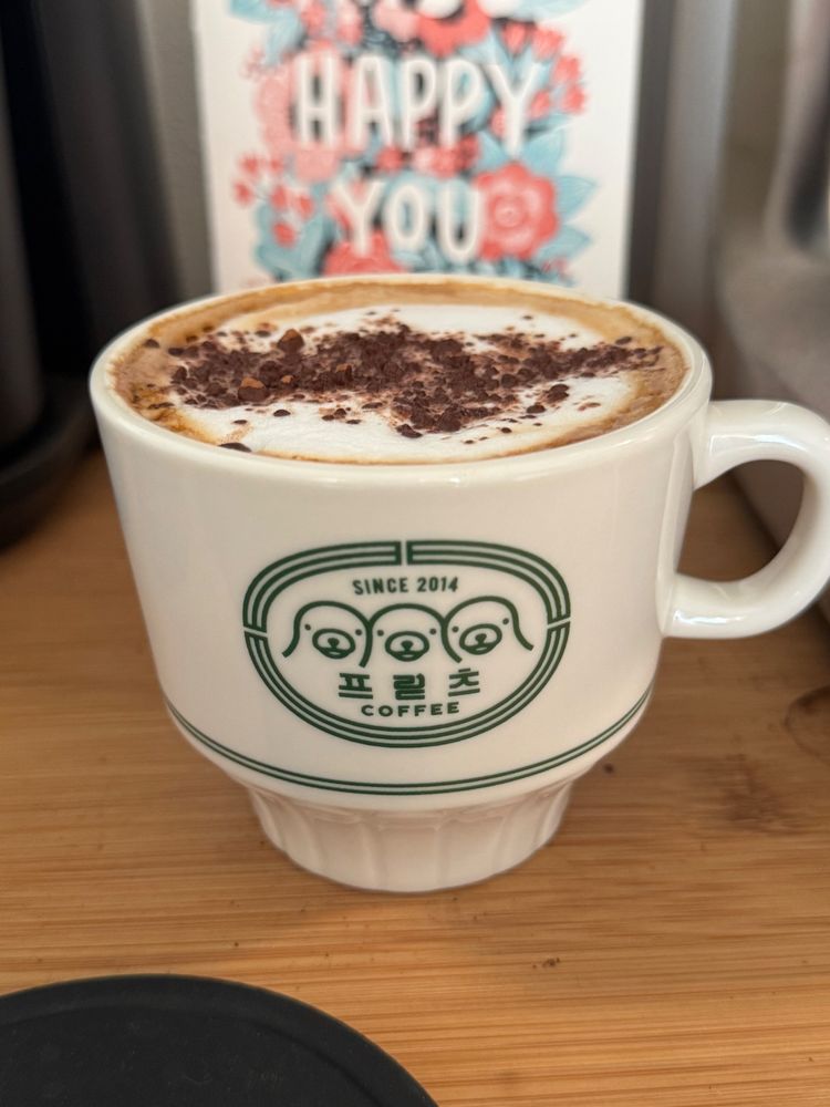 A cappuccino dusted with cacao powder, in a small white Fritz Coffee Company cup - the logo is green, three seals looking out from a circle
