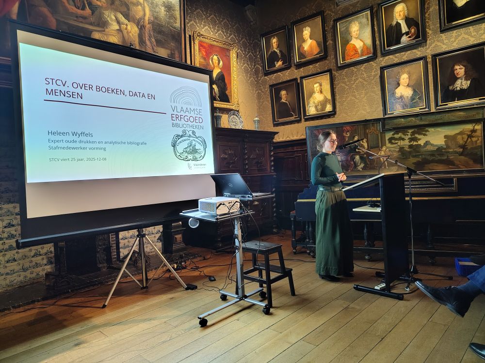 A woman (Heleen Wyffels) giving a presentation in a museum room with old portraits on the walls.