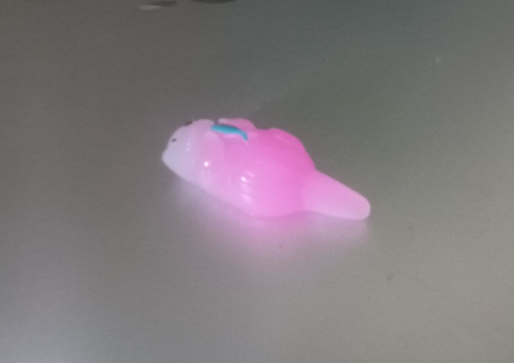 a tiny pink plastic sea otter on its back holding a feesh