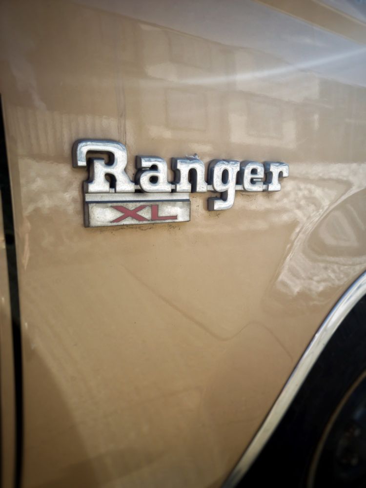 A 1970s Ford Ranger logo with the reflection of a new building in the gold paint.