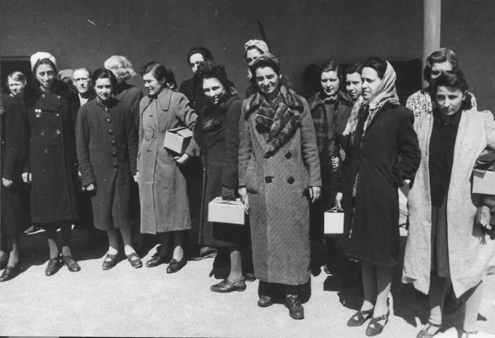 Grupo de mujeres con abrigos y paquetes blancos. Acaban de ser liberadas de Ravensbruck 