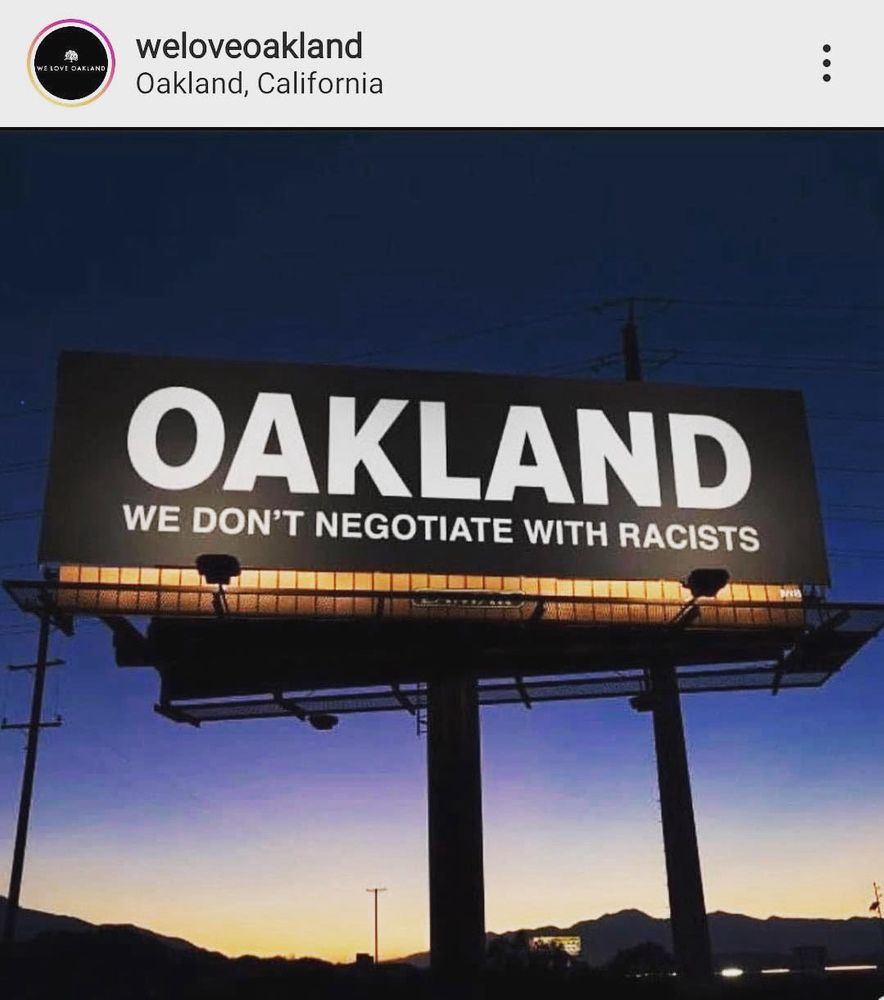 Digital Billboard graphic in front of a twilight sky that says “Oakland we don’t negotiate with racists” 
Likely designed by We Love Oakland, not a real billboard 