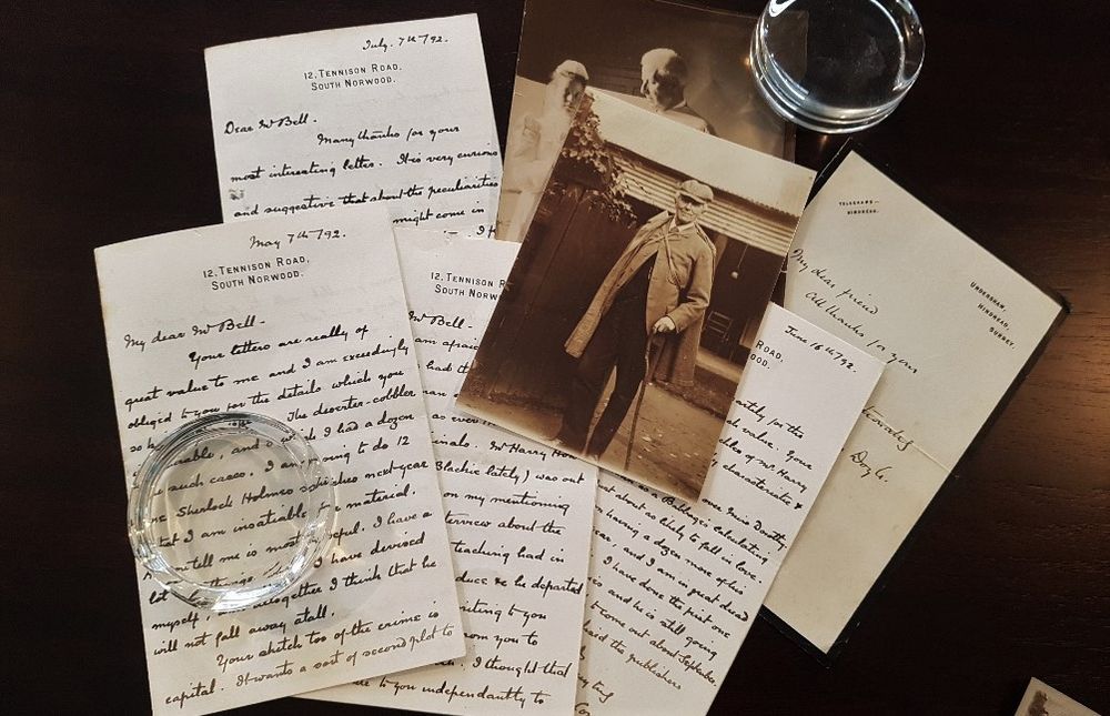 A photograph of Joseph Bell in deerstalker outfit on top of a photograph of Bell with a nurse and four letters from Arthur Conan Doyle, with two glass paperweights.