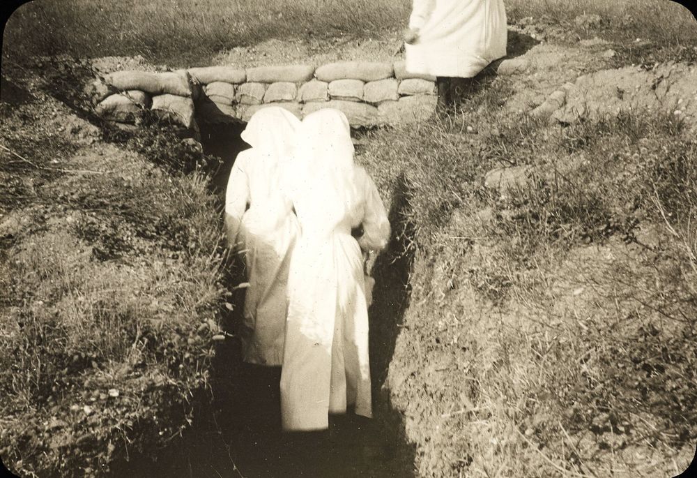 Black and white lantern slide showing the back of two nurses walking towards the end a trench and a partial view of another nurse above.