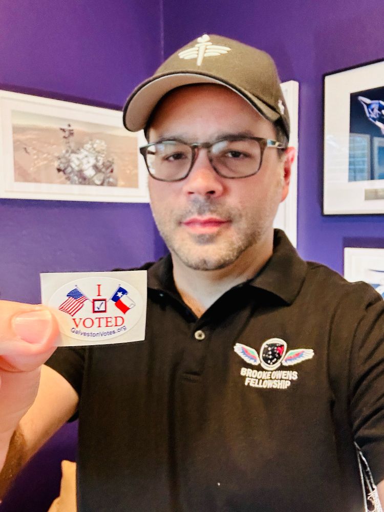 “I voted” sticker selfie. Wearing my Patti Grace Smith Fellowship and Brooke Owens Fellowship swag, standing in front of pictures of a few spacecraft I’ve worked on.