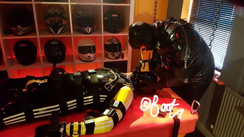 Total rubber encased pup tending to another rubber pup who is strapped down to a bondage table
