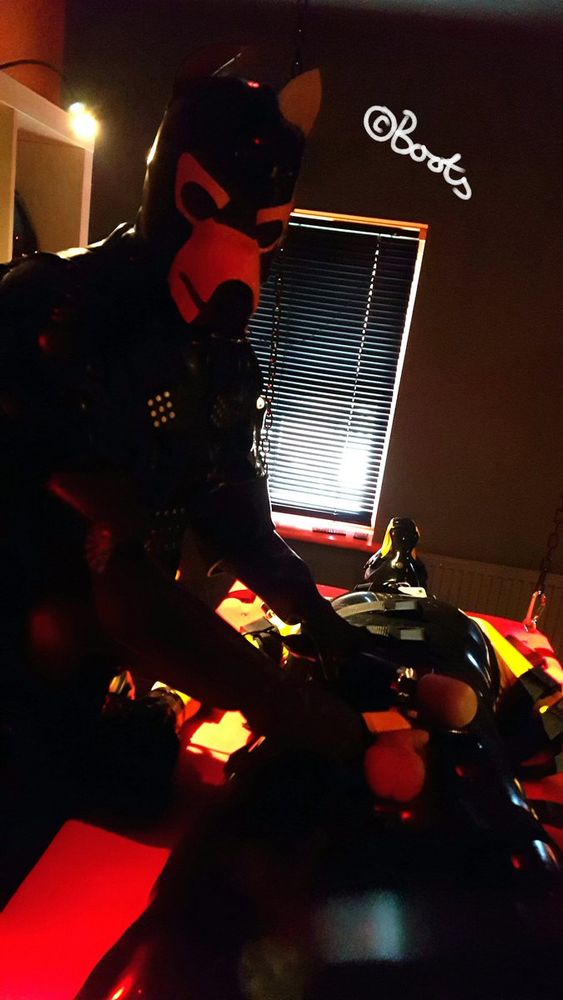 Total rubber encased pup tending to another rubber pup who is strapped down to a bondage table