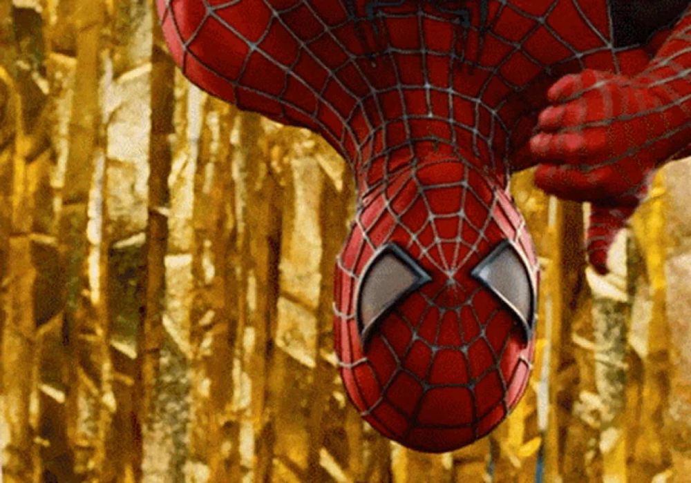 a close up of a spider man hanging upside down in front of a gold background