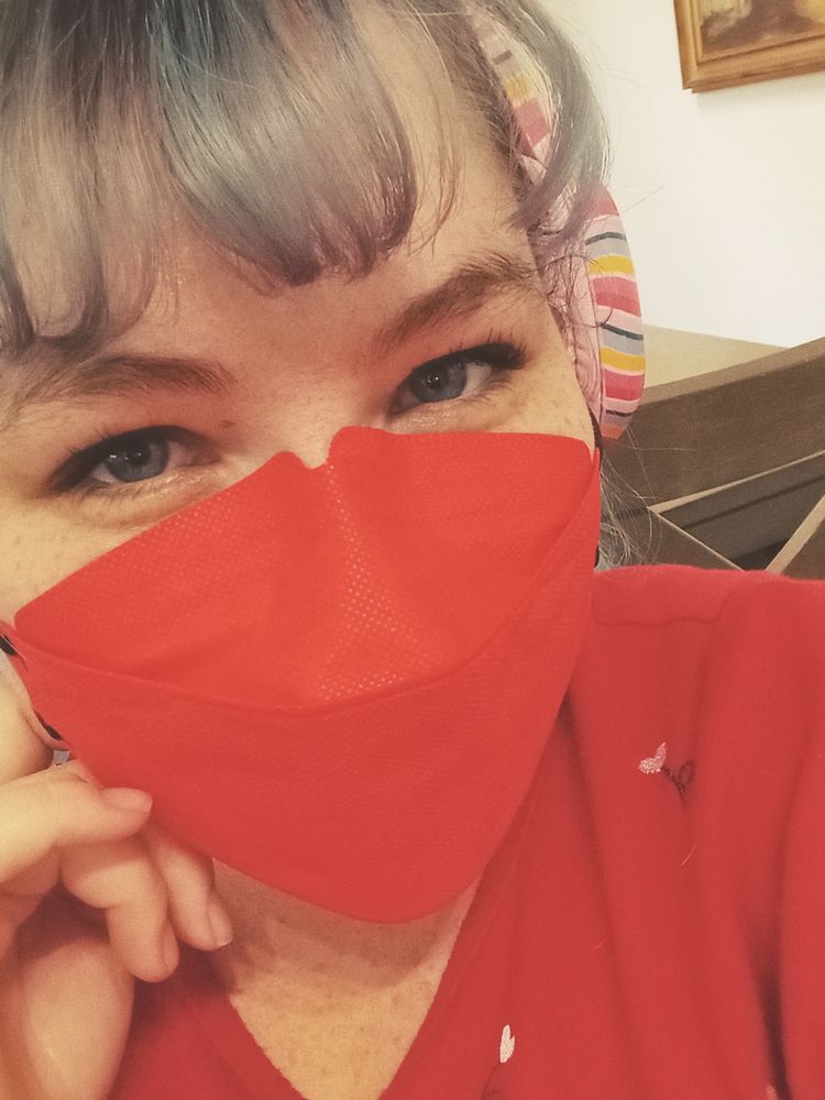 beau, a white person with freckles, blue eyes, and blue hair wearing a red face mask, red shirt and multi colored headphones. 