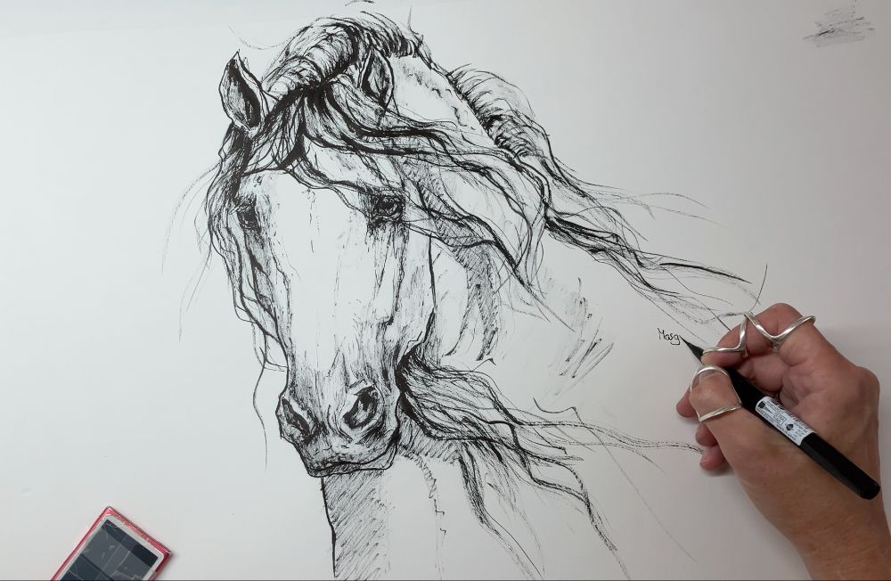 A sketch with a brushpen on white paper. An Andalusian horse with flowy manes. You can see an ipos lying on the paper and a hand signing the sketch with a name. 