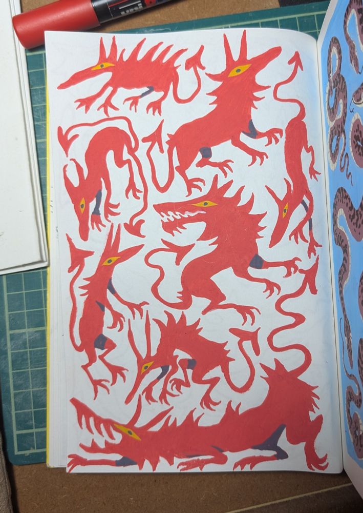 a photograph of a sketchbook page with simple red dog-like creatures with yellow eyes in a variety of poses. 