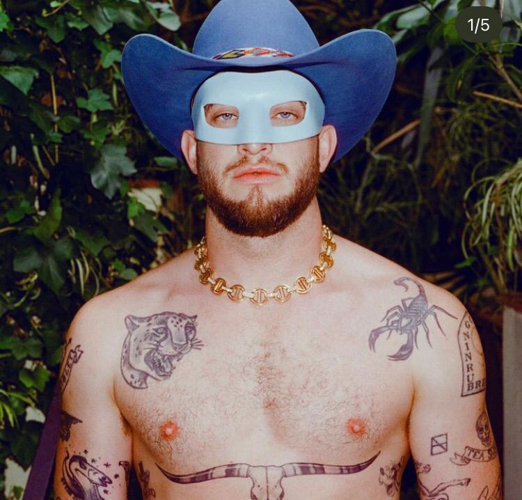 Orville Peck oberkörperfrei. Unter seiner Brust verläuft ein Tattoo: die Hörner eines Auerochsen, die genau den Bereich bedecken, wo typischerweise Mastektomie Narben verlaufen.