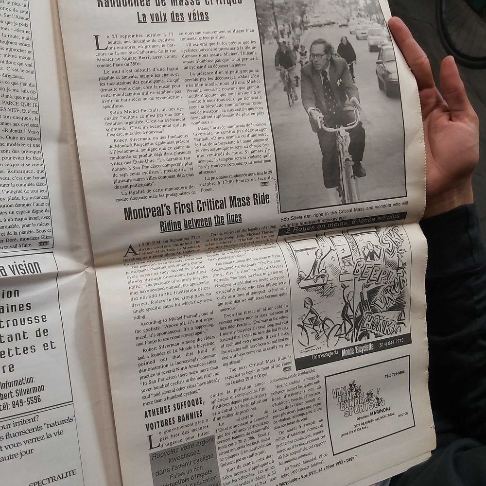 Photo d'une page de journal annonçant la première Masse Critique de Montréal. Le journal comprends une version française et anglaise de l'article. À la droite de la page, il y a une photo de quelques cyclistes en formation de Masse Critique, et en dessous un dessin d'une masse critique dans un style caricatural.