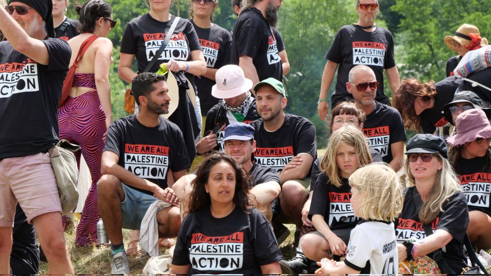 Group of people sat on in a hill in "we are all Palestine Action" t-shirts.