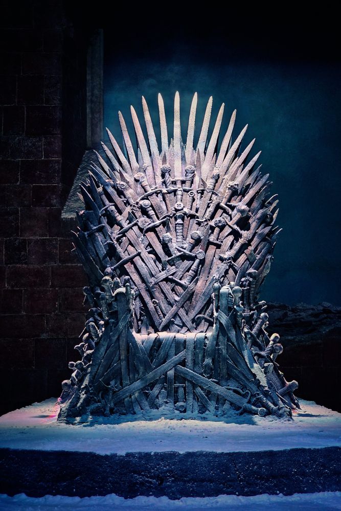 A detailed shot of the iconic Iron Throne from Game of Thrones, constructed from numerous swords and sitting on a slightly snowy platform against a dark, moody background.