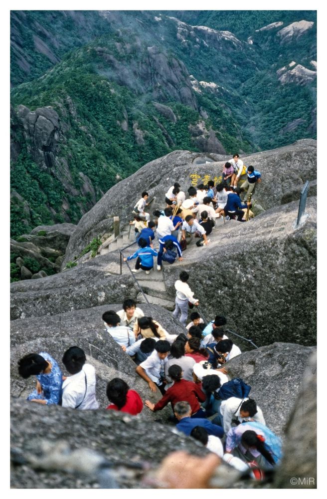 Aufstieg auf schmalen, steilen Wegen durch den Fels im Huangshan, beliebt bei vielen Touristen (in diesem Fall 1986 chinesische). Im Hintergrund das Tal aus dem der Aufstieg beginnt