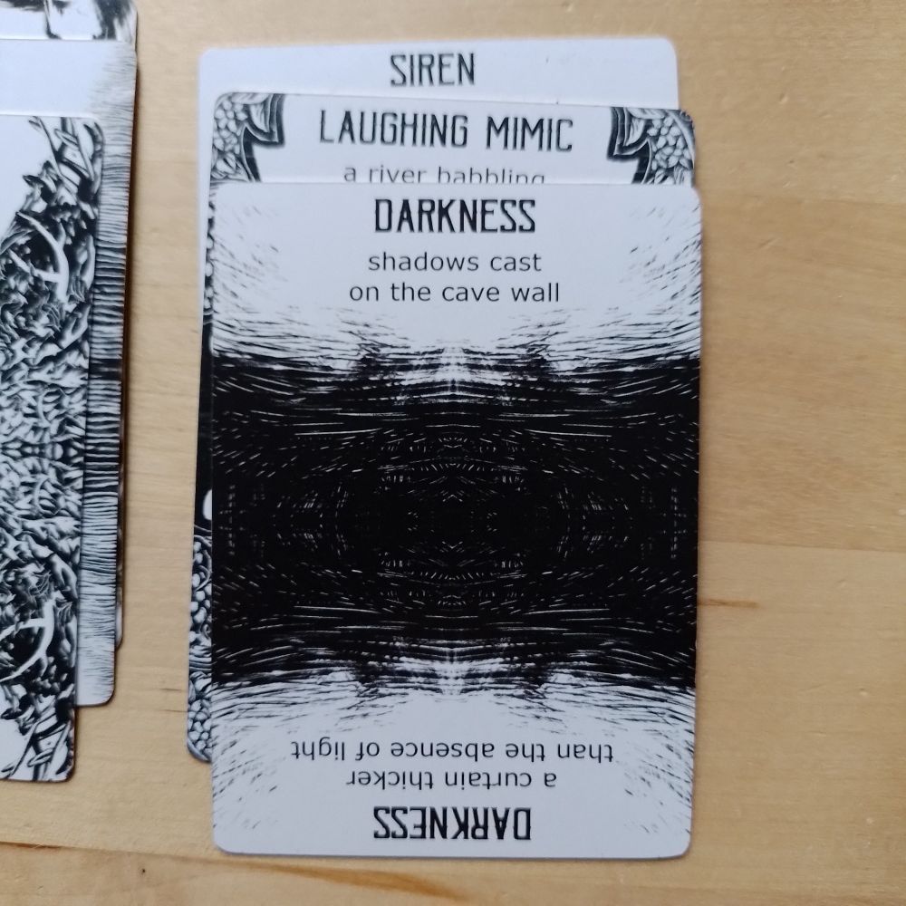 A stack of Spindlewheel cards: Siren, under Laughing Mimic, under Darkness: shadows cast on the cave wall, or reversed, a curtain thicker than the absence of light