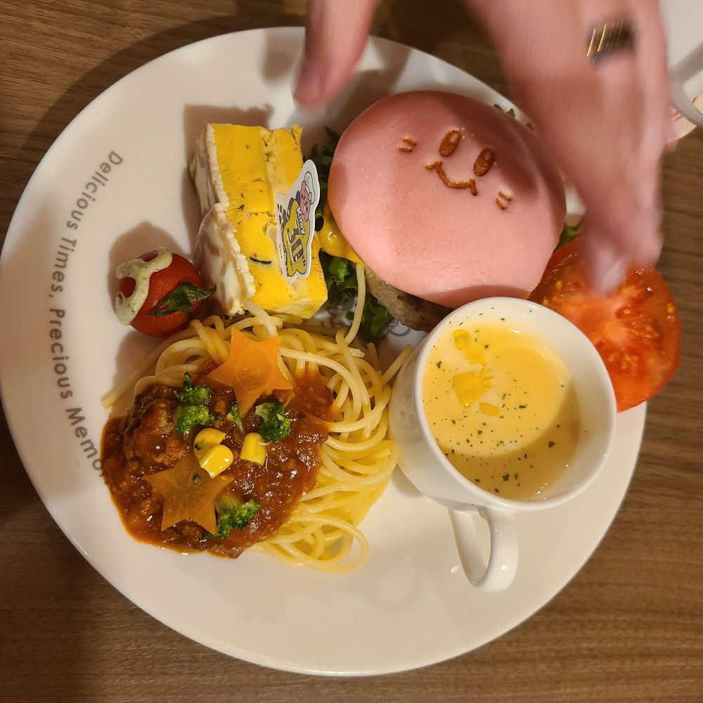 A meal from Kirby Cafe in Japan. Includes a cup of Corn Soup, a Kirby-faced burger, and a side of spaghetti.