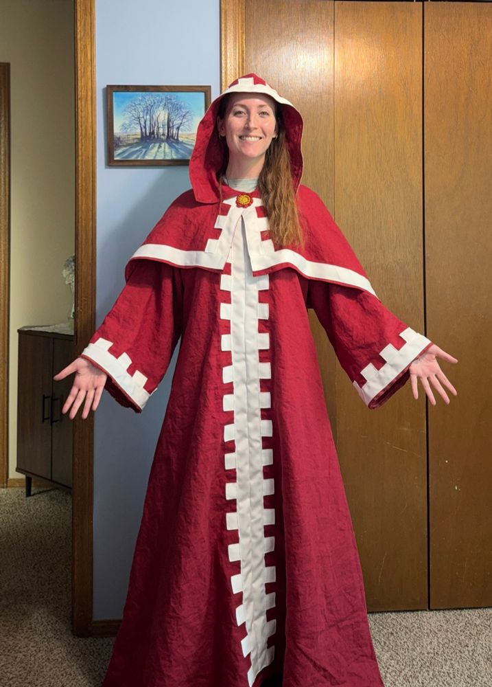 Smiling woman wearing a long red robe with white cog trim from the Warhammer technological faction, the Adeptus Mechanicus. 