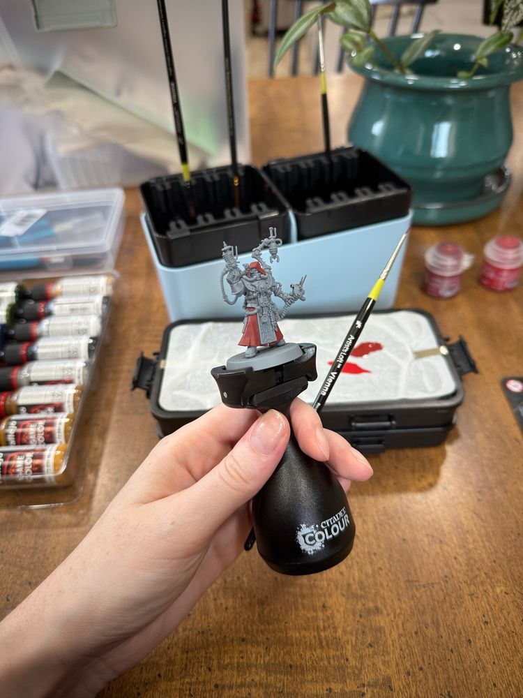 A small war gaming miniature of a tech priest with painting supplies around it. 
