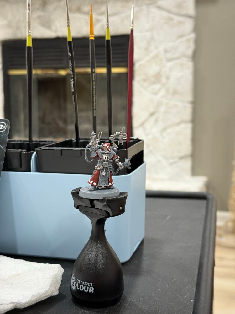 A half-painted Warhammer miniature of a tech priest in red robes.